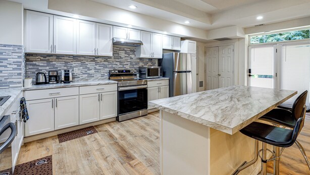 A modern kitchen with white cabinets, a marble countertop, stainless steel appliances, and a wooden floor.