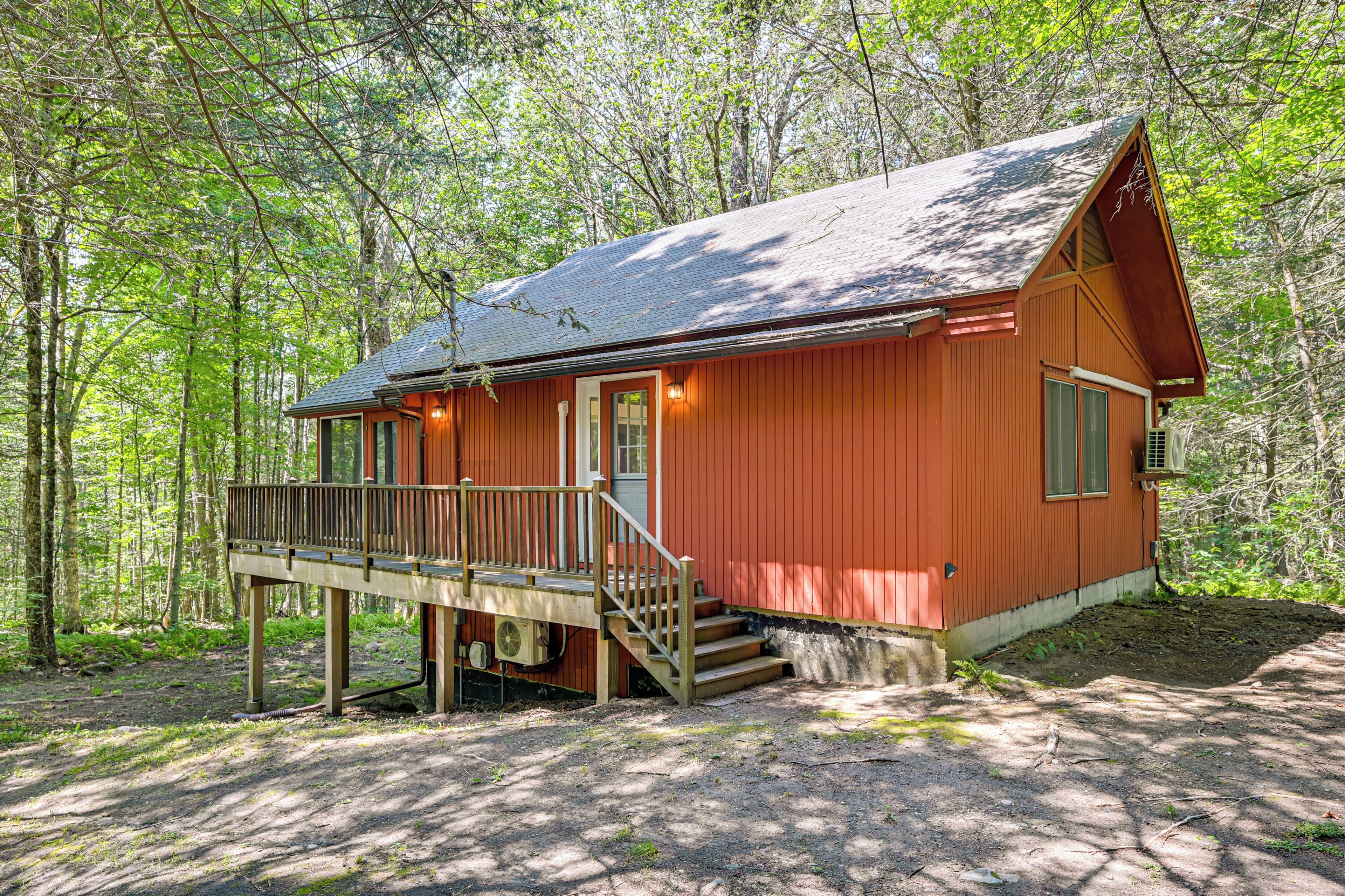 A cabin with a wooden deck, a front porch, and a small staircase leading to the entrance.