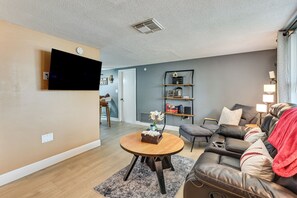 A living room with a flat-screen TV mounted on the wall, a round wooden coffee table, a leather sofa with a red throw blanket, and a bookshelf with decorative items. - Private Pool! Port Richey Home Near Coast & Trails (Port Richey)