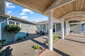 A covered patio area with a wooden ceiling, a seating arrangement, and a view of a house with a green exterior.