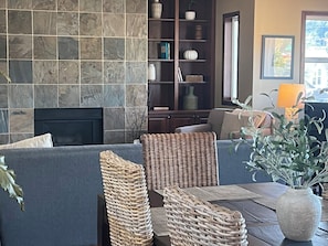 A living room with a stone fireplace, a sofa, wicker chairs, a bookshelf, and a vase with plants.