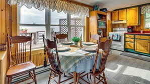 A dining area with wooden chairs, a table set for four, and a view of the outdoors. - Sunset Views & Deck: Lake Champlain Cottage! (Swanton)