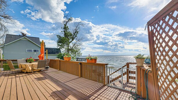 A wooden deck with a table and chairs, potted plants, and a view of the water. - Sunset Views & Deck: Lake Champlain Cottage! (Swanton)