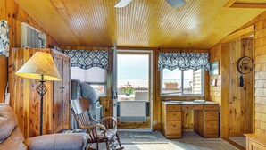 A cozy cabin interior with a rocking chair, a desk, and a view through a door. - Sunset Views & Deck: Lake Champlain Cottage! (Swanton)