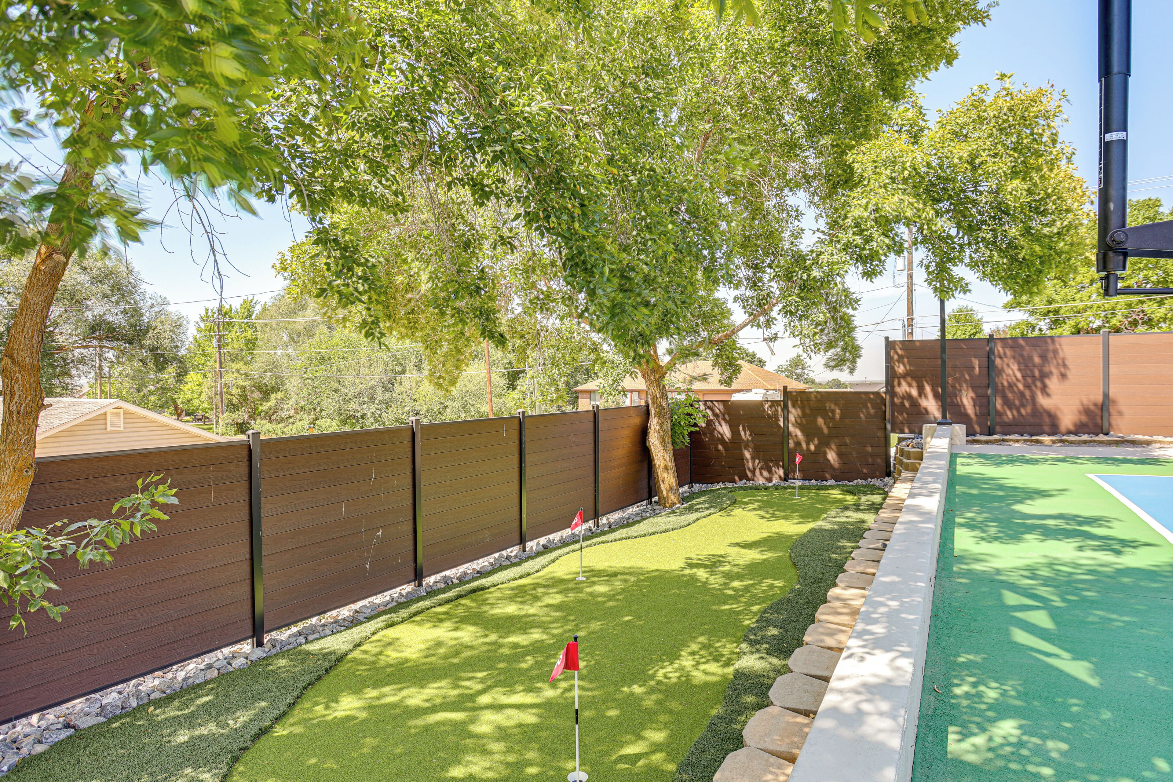 A backyard with a green artificial turf, a wooden fence, and a flag.