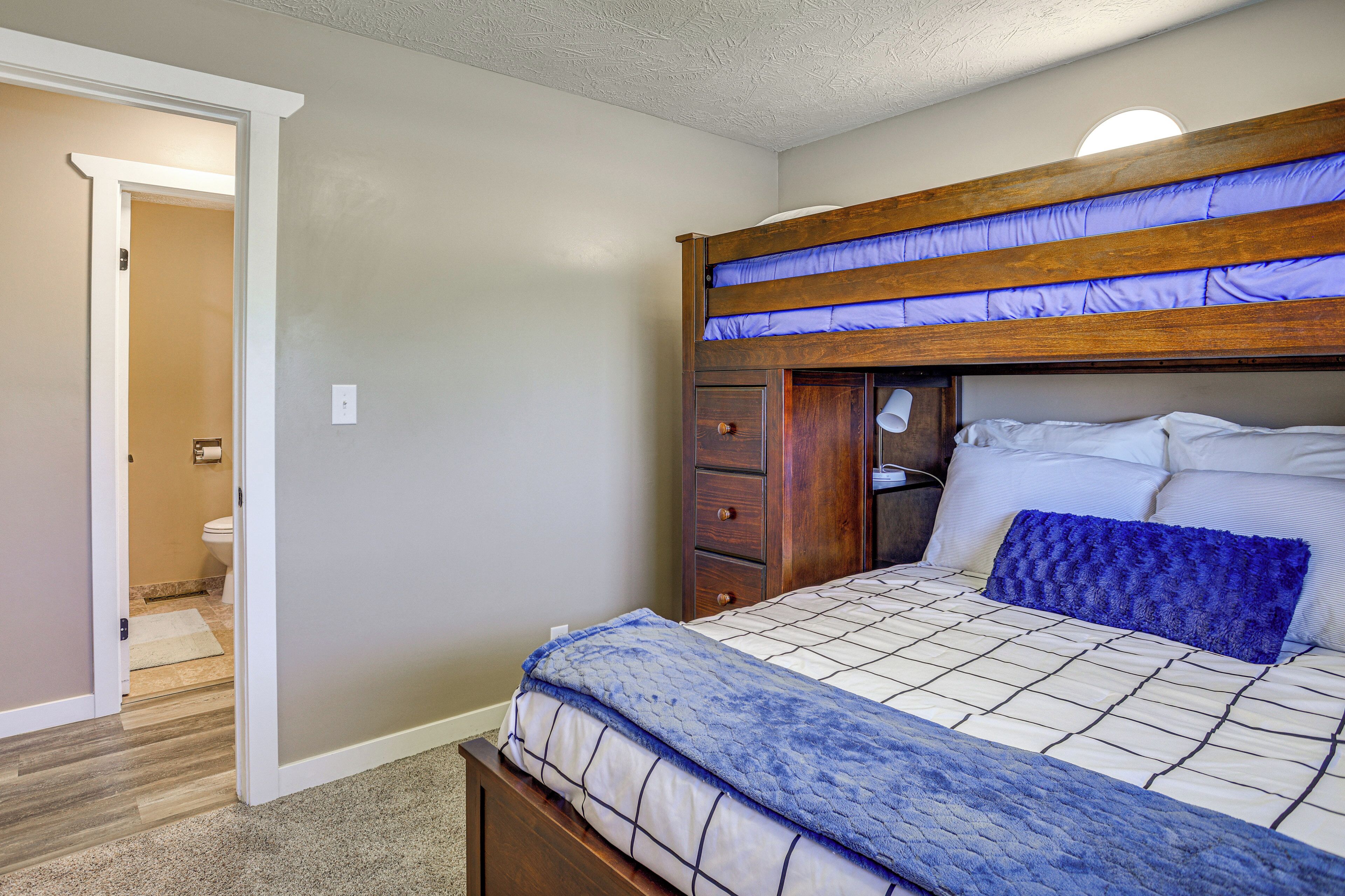 A bedroom with a bunk bed, a bedside table, a drawer unit, and a carpeted floor.