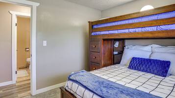 A bedroom with a bunk bed, a bedside table, a drawer unit, and a carpeted floor.