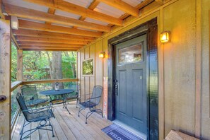 Una terraza de madera con una puerta negra, dos sillas de metal y una mesa.