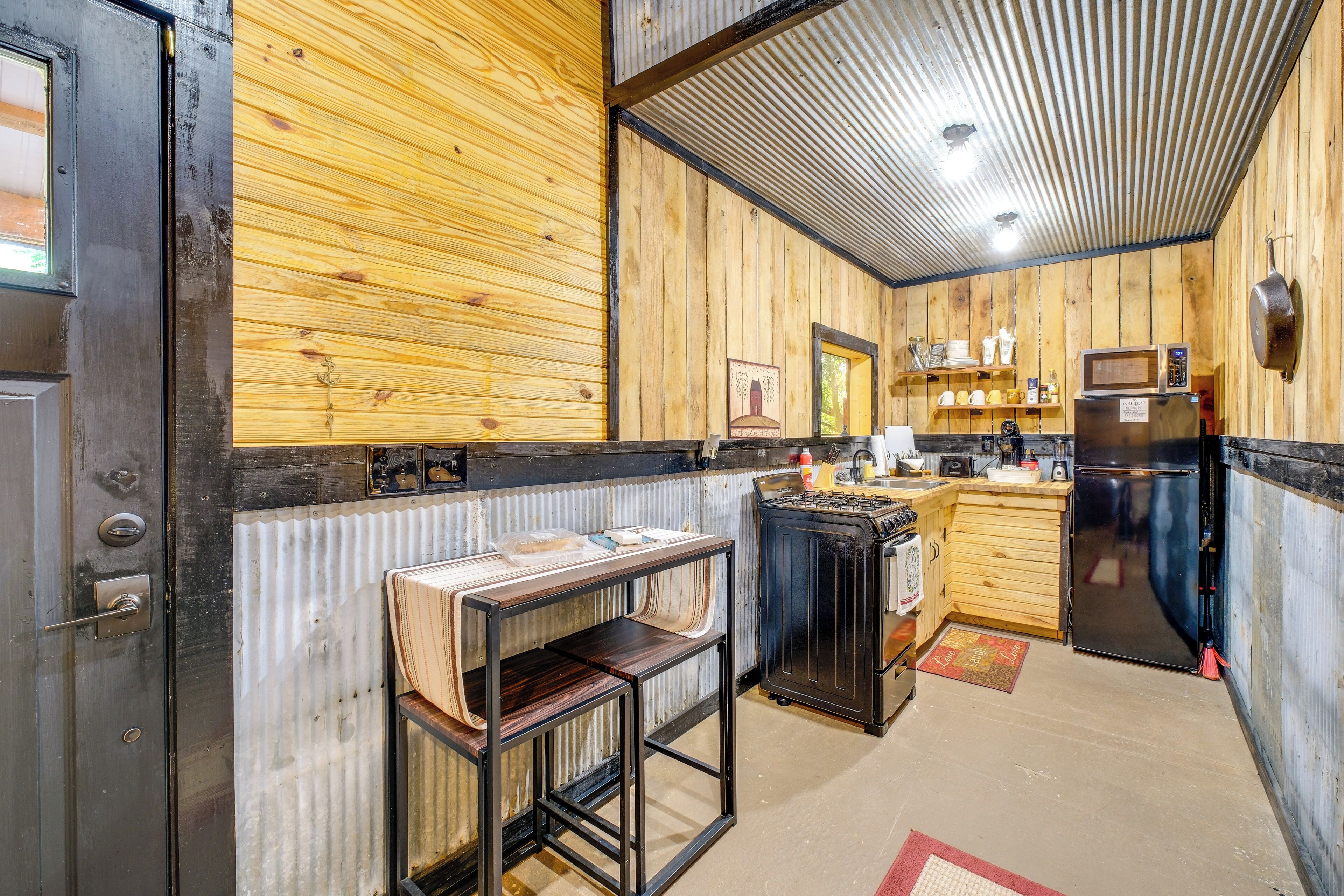 Une cuisine rustique avec des murs en bois, un réfrigérateur noir, un four à micro-ondes et une petite table.