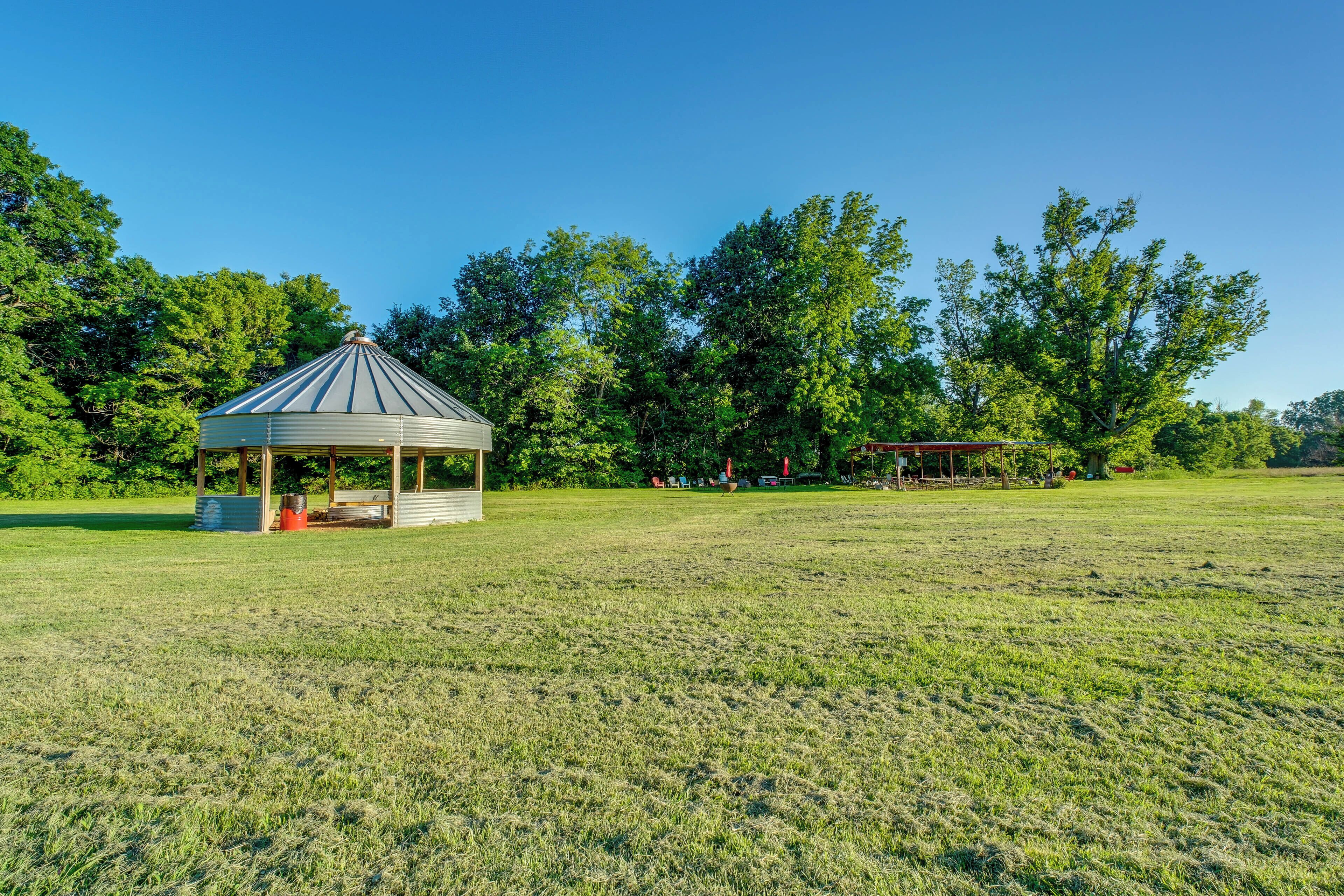 A gazebo in a grassy field with trees in the background.