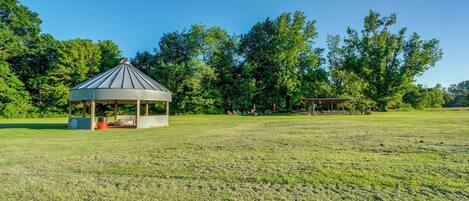 A gazebo in a grassy field with trees in the background.
