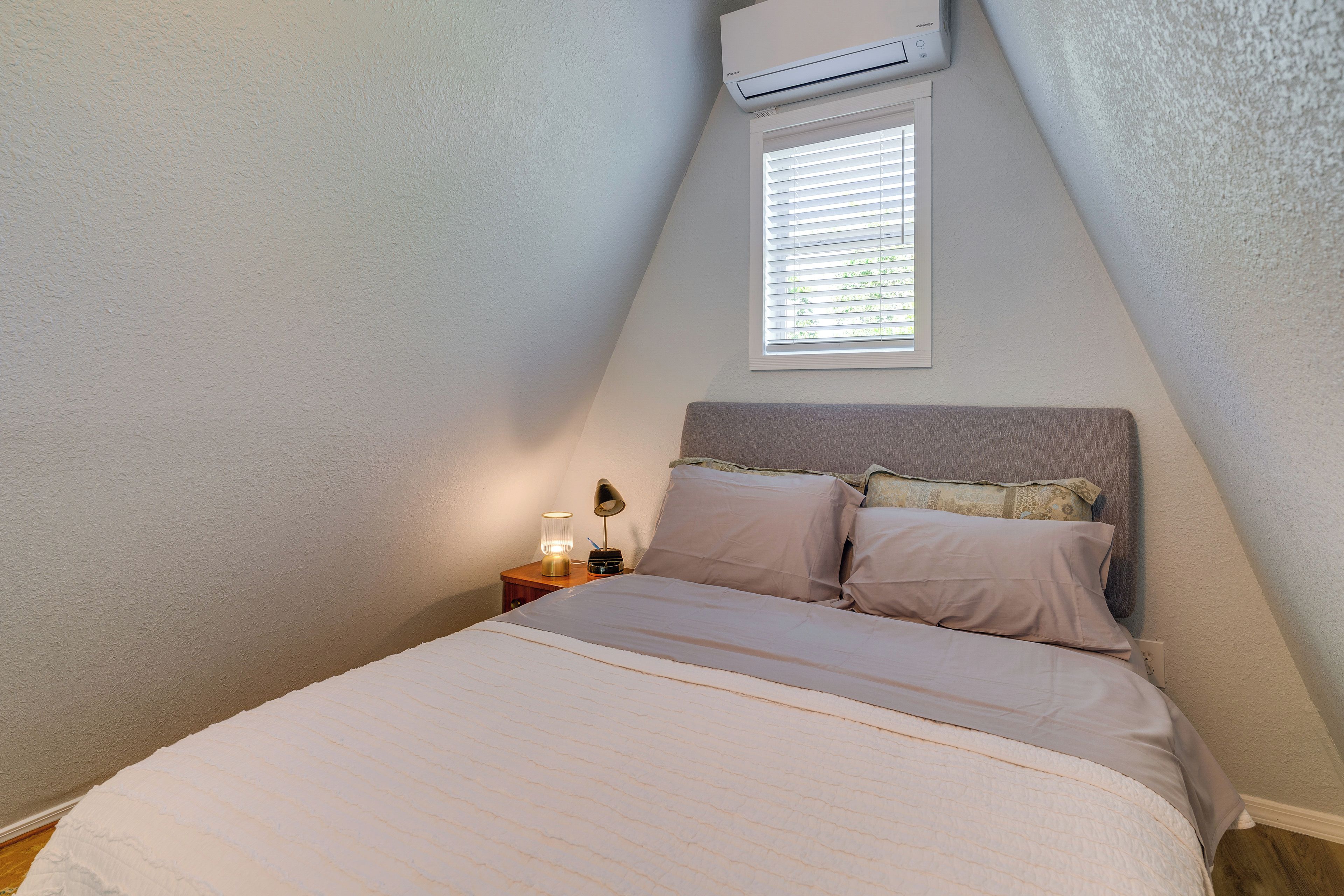 Un dormitorio con cama, lámpara de noche y unidad de aire acondicionado en la pared.