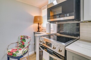 A compact kitchen with a microwave, oven, and a chair with floral upholstery.