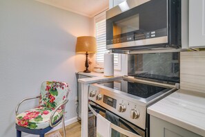 A compact kitchen with a microwave, oven, and a chair with floral upholstery.