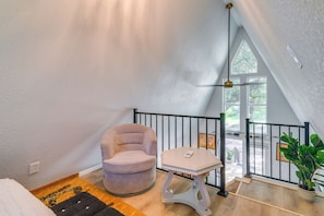 A room with a high ceiling, a chair, a small table, a railing, and a potted plant.