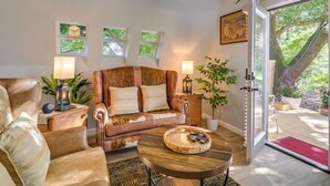 Una sala de estar acogedora con un sofá de cuero, una mesa de centro de madera y vistas a un jardín a través de un ventanal.