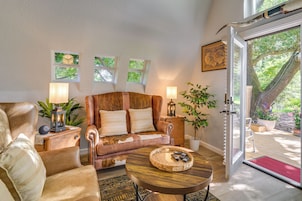 A cozy living room with a leather sofa, a wooden coffee table, and a view of a garden through a glass door.