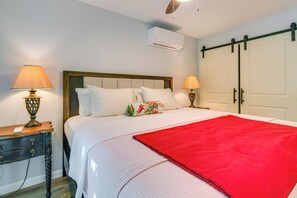 A neatly made bed with a red blanket, two bedside lamps, a wooden nightstand, and a sliding closet door.