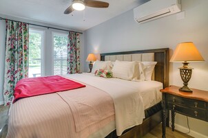 Una cama bien hecha con un edredón rojo, dos lámparas de noche y una mesita de madera.