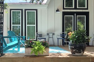 A covered patio with a blue chair, a white planter with green plants, a large potted plant, and a table with chairs.