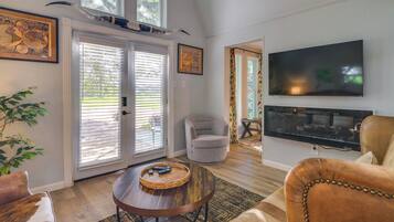 A living room with a television, a round coffee table, a sofa, a chair, and a large window with blinds.