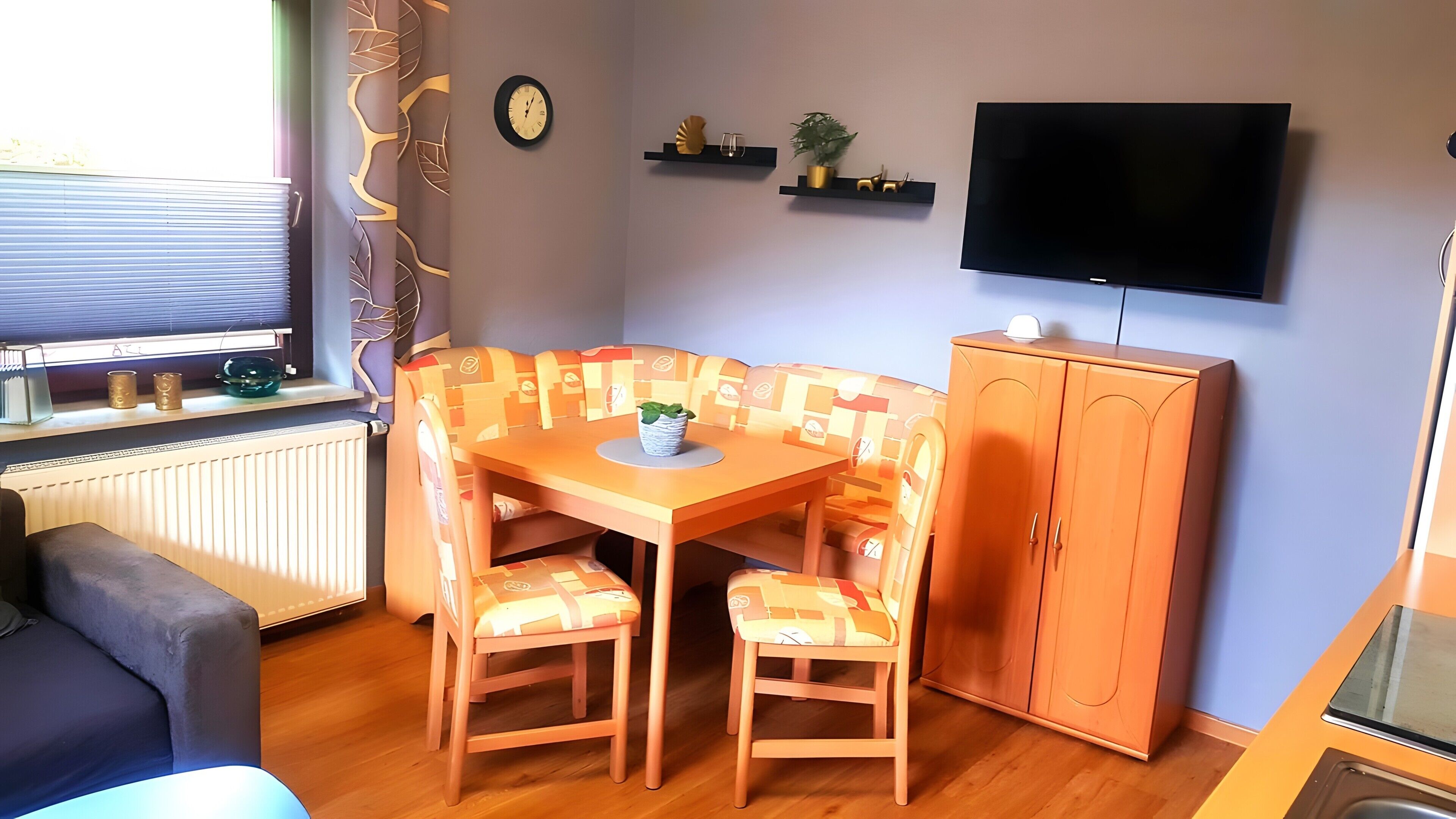 A cozy living room with a wooden table, two chairs, a sofa, a TV, and a cabinet.