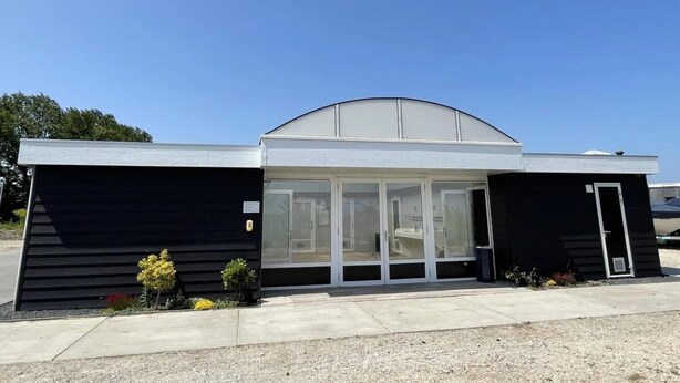 Un bâtiment moderne doté d’un toit incurvé, de grandes portes vitrées et d’une façade noire.