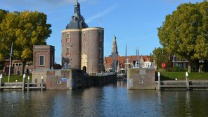 Un bâtiment historique doté d’une tour imposante et d’une annexe plus petite, situé au bord d’un plan d’eau paisible.