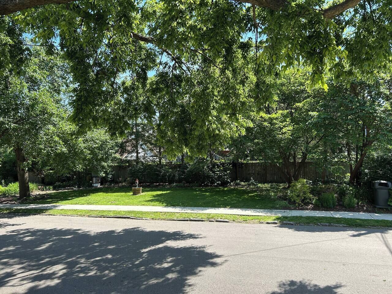 A residential street with a sidewalk, a grassy area, and trees.