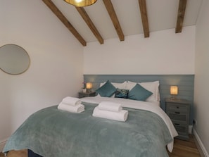 A bedroom with a bed, bedside tables, a nightstand, a mirror, and a wooden ceiling. - Cosy Cottage (Bath)