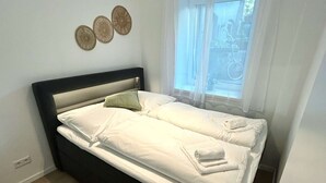 A neatly made bed with white linens, a dark headboard, and a window with sheer curtains. - Stylish Apartment in Eimsbuettel Hamburg for 4 (Hamburg)