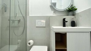A modern bathroom with a glass shower enclosure, a toilet, a sink with a mirror, and a small plant. - Stylish Apartment in Eimsbuettel Hamburg for 4 (Hamburg)