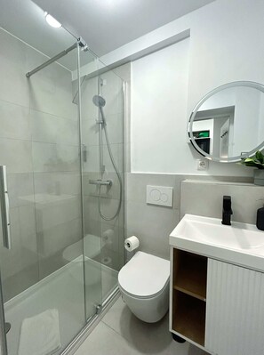 A modern bathroom with a glass-enclosed shower, a white toilet, a sink with a black faucet, and a mirror with a round frame. - Stylish Apartment in Eimsbuettel Hamburg for 4 (Hamburg)