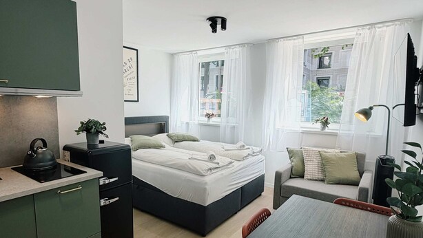 Een moderne kamer met een bed, een bank, een eettafel en een keukenhoek.