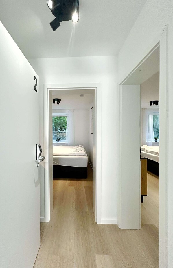 A modern bedroom with a bed, a window, and a door leading to another room.