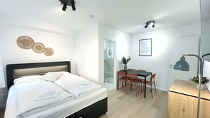Une chambre à coucher comprenant un lit, un bureau et une chaise, un petit meuble et une lampe fixée au mur.