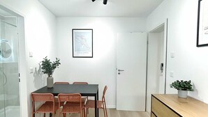 Un espace repas moderne comprenant une table, des chaises, un luminaire au plafond, un tableau encadré et une commode en bois.