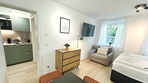 Un espace de vie compact comprenant un coin cuisine, un coin repas, un canapé, une télévision et un lit.