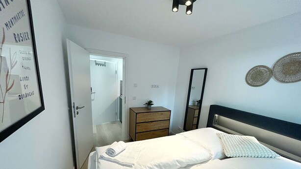 Une chambre à coucher comprenant un lit, une commode, un miroir et une porte donnant sur une autre pièce.