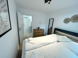 A bedroom with a bed, a dresser, a mirror, and a door leading to another room.