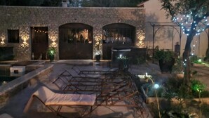 A courtyard with lounge chairs, a pool, and a stone building with arched doorways. - Gite in the Vines Le Borie at Mas des Armouriers, with Pool (Violès)