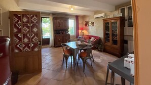 An open-plan living and dining area with a kitchen, a dining table with chairs, a red sofa, and a cabinet with glass doors. - Gite in the Vines Le Borie at Mas des Armouriers, with Pool (Violès)