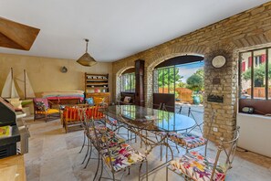 A spacious room with a glass dining table surrounded by chairs, a wooden bookshelf, and a sailboat model. - Gite in the Vines Le Borie at Mas des Armouriers, with Pool (Violès)