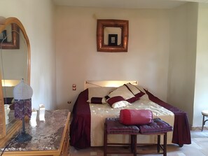 Un dormitorio con una cama, un espejo, una mesita y un taburete.