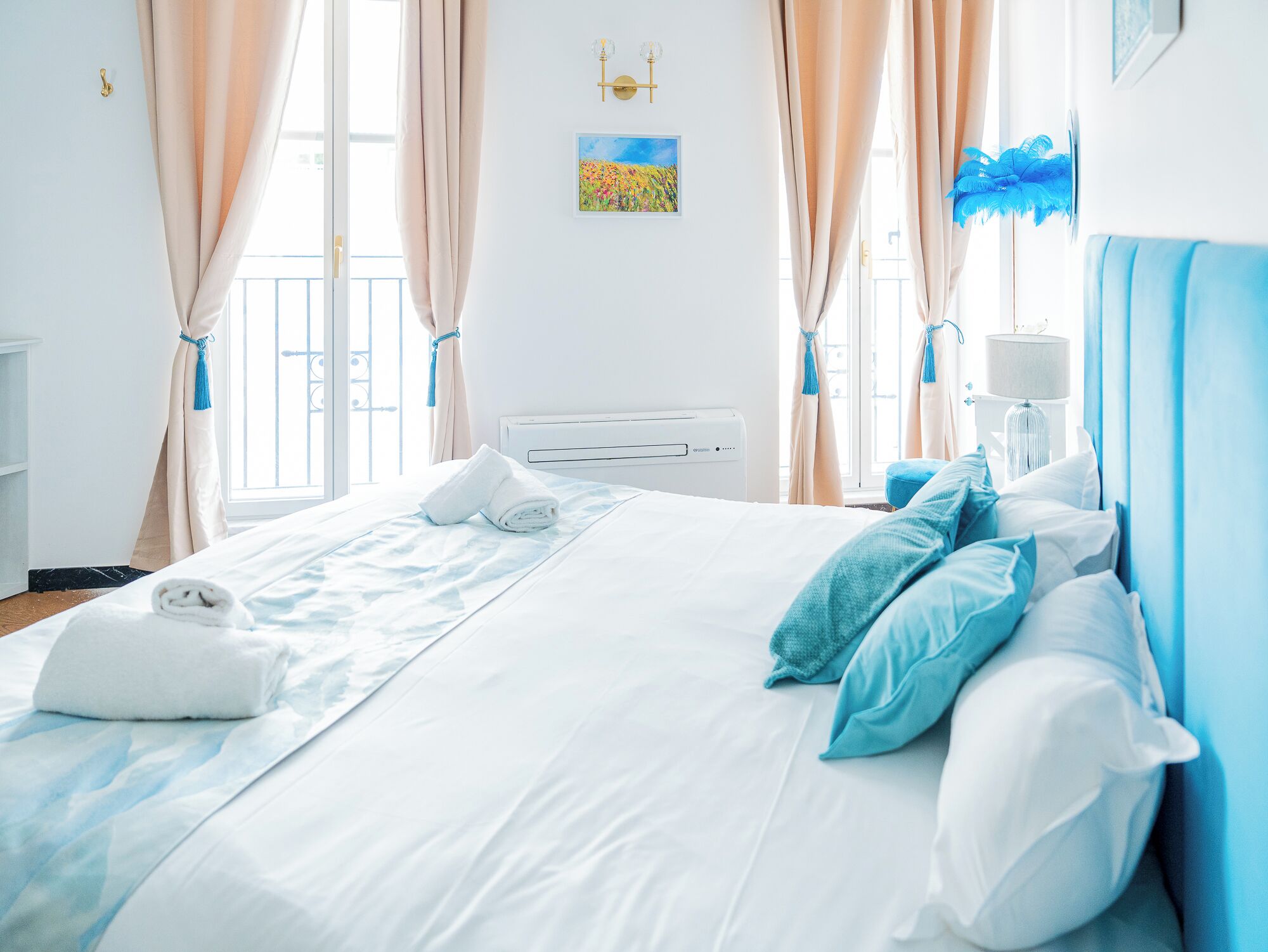 A hotel room with a bed, curtains, a radiator, a wall-mounted lamp, and a window with a view.