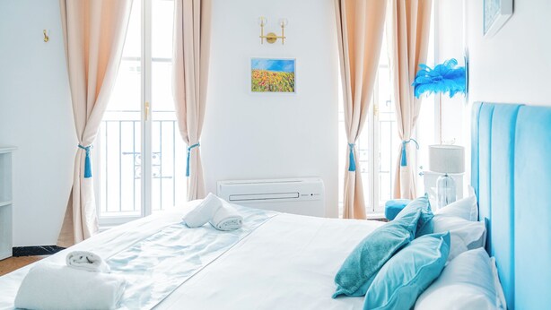 Ein Hotelzimmer mit Bett, Vorhängen, Heizkörper, Wandlampe und einem Fenster mit Blick.