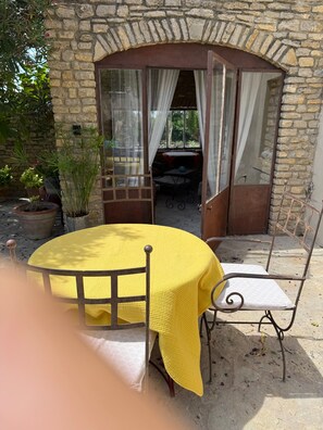 Ein Steingebäude mit einem gelben Tisch und Stühlen, einer kleinen Terrasse und Topfpflanzen.