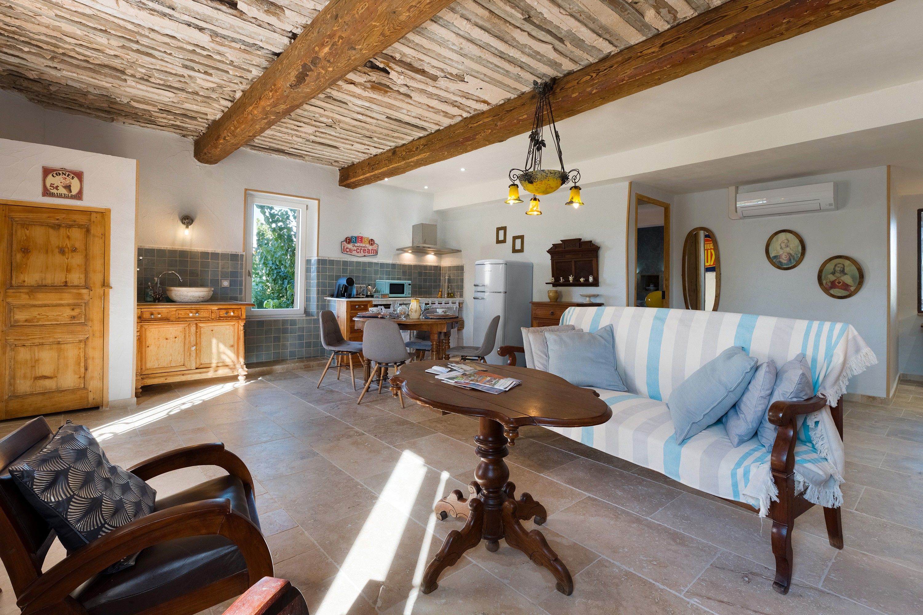 A spacious living area with a wooden dining table, a sofa with striped cushions, and a kitchen in the background.