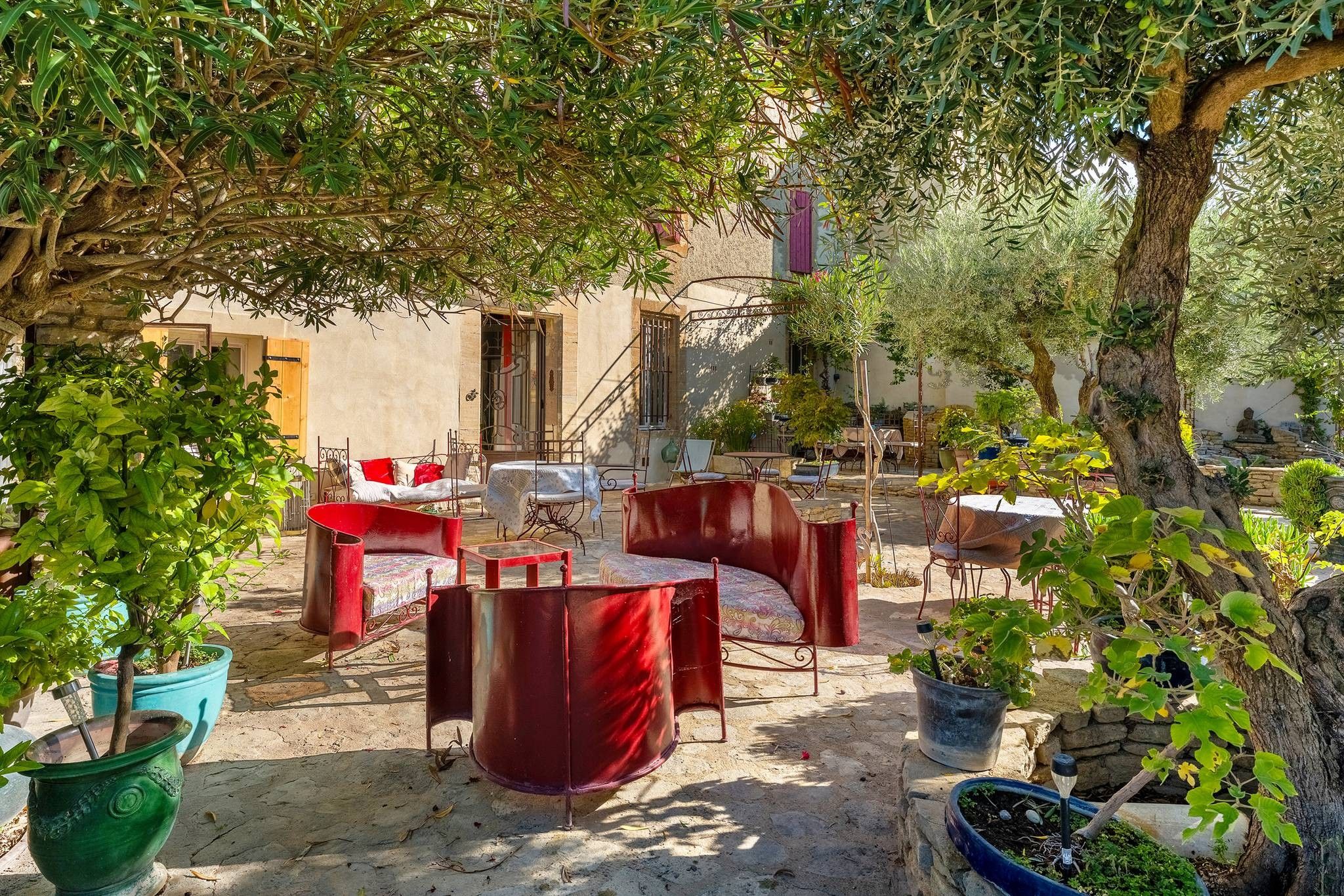An outdoor seating area with red furniture, surrounded by potted plants and trees.
