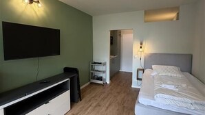 Ein Zimmer mit einem Bett, einem Schreibtisch, einem Fernseher und einer Tür zu einem anderen Raum.